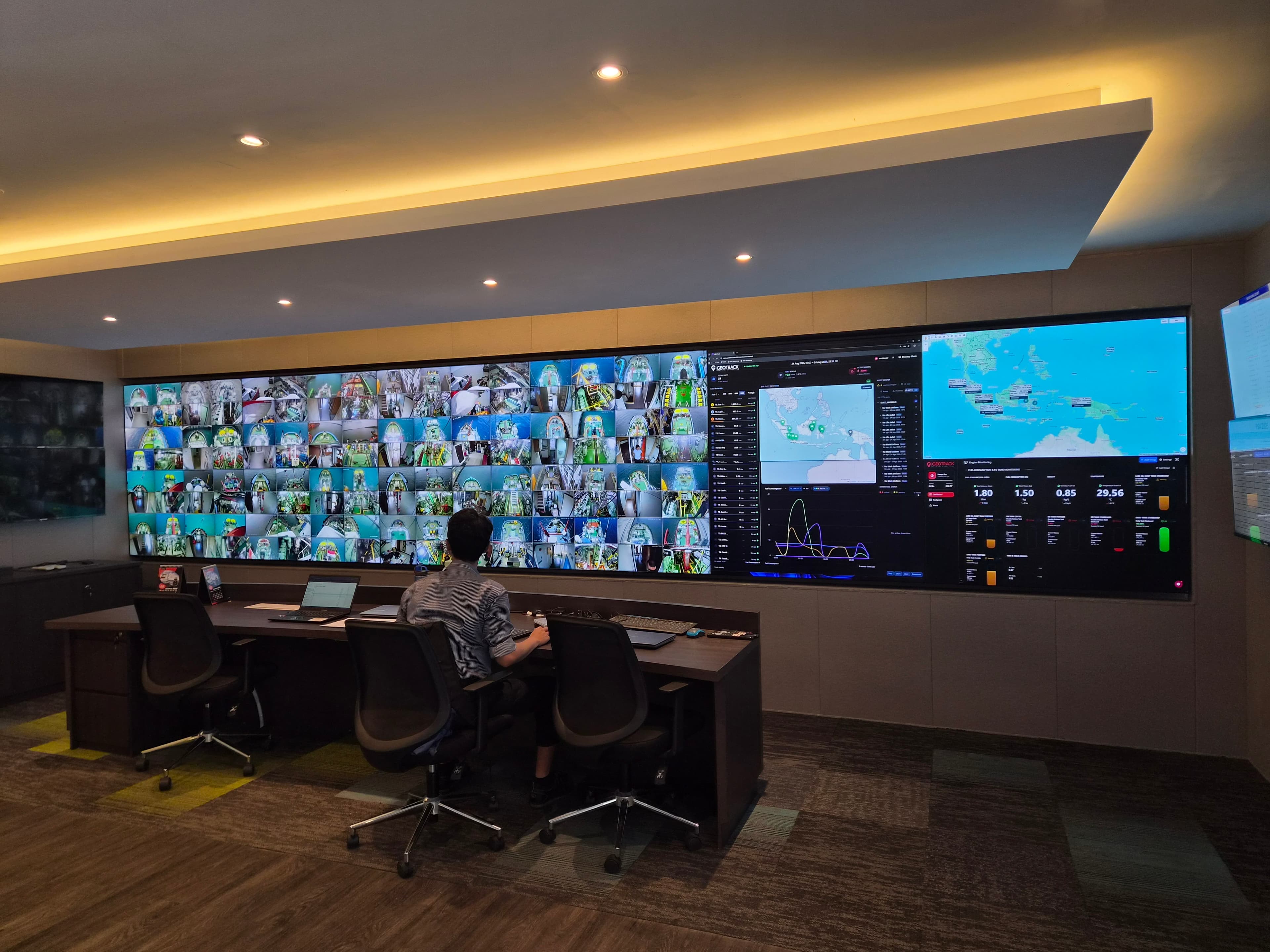 An operator at the Moda Holdings command centre, facing a wall of screens showing vessel CCTV feeds, telemetry dashboards and fleet maps.